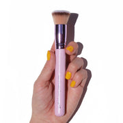 shiny purple flat-top foundation kabuki in hand with yellow fingernails - complexion brush- half caked