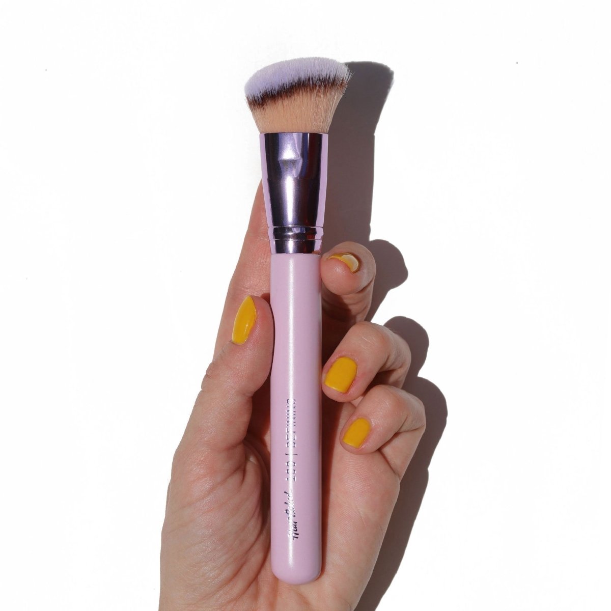 shiny purple angled contour brush in hand with yellow fingernails - defining - half caked makeup