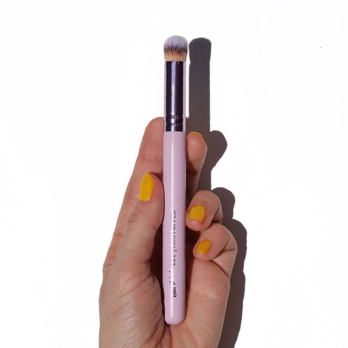 shiny purple concealer brush in hand with yellow nails - Mini Buffer Brush - Half Caked